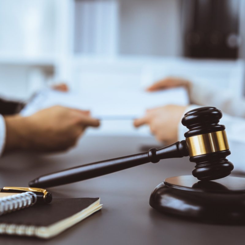 Focus closeup wooden gavel on blur background of lawyer colleagues or drafting legal documents on their workplace at law firm office. Hammer of justice for righteous and equality judgment. Equilibrium