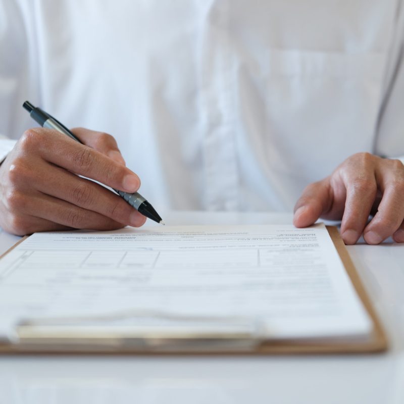 A man is writing on a piece of paper with a pen. He is wearing a white shirt and he is focused on his writing. Concept of concentration and determination as the man puts pen to paper